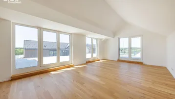 Heller, geräumiger Raum mit Holzboden und großen Fenstern, die viel Tageslicht hereinlassen.