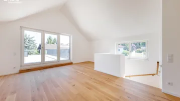 Heller Dachgeschossraum mit Holzboden, großen Fenstern und Zugang zu einem möglichen Balkon oder einer Terrasse.
