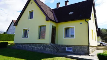 Gelbes Einfamilienhaus mit Satteldach, Steinsockel und gepflegtem Vorgarten unter blauem Himmel.