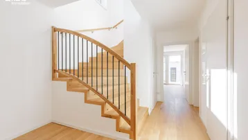 Heller Flur mit moderner Holztreppe und Parkettboden, der zu weiteren Räumen führt.