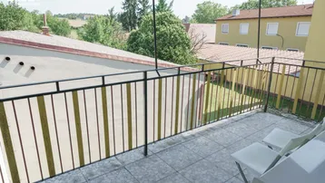Balkon mit Fliesenboden und Metallgeländer, bietet Blick auf die umliegenden Gebäude und Grünflächen.
