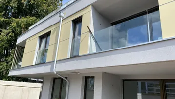 Moderne Gebäudefassade mit großen Fenstern, Glasbalkonen und heller Verkleidung.