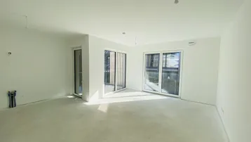 Heller, unmöblierter Wohnbereich mit großen Schiebetüren und Betonboden, bereit für den Ausbau.