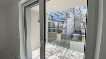 Heller Innenraum mit Zugang zu einem modernen Balkon und Blick auf die umliegenden Gebäude.