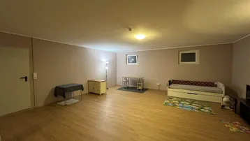 Geräumiger Mehrzweckraum mit Laminatboden und einfacher Möblierung, bereit zur individuellen Gestaltung.