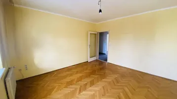 Heller Raum mit Fischgrätparkettboden und gelben Wänden, mit Zugang zu einem weiteren Zimmer.
