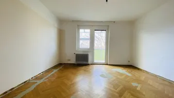 Heller Raum mit Fischgrätparkett, Heizkörper und Zugang zu einem Balkon, der eine Renovierung benötigt.