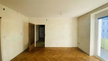 Leeres Wohnzimmer mit Fischgrätparkett und Zugang zum Balkon, bereit zur Renovierung.