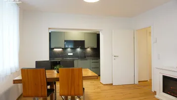 Heller Wohn- und Essbereich mit Holzboden, modernem Kamin und Blick in die integrierte Küche.