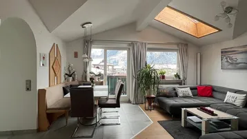 Geräumiger Wohn- und Essbereich mit Dachschrägen, Holzboden und Zugang zum Balkon, hell durch Dachfenster.