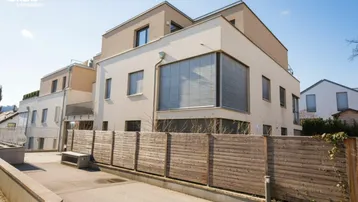 Modernes Mehrfamilienhaus mit heller Fassade und großen Fenstern in sonniger Umgebung.