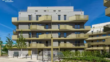 Moderne Wohnanlage mit mehreren Etagen, Balkonen und gepflegter Außenanlage unter blauem Himmel.