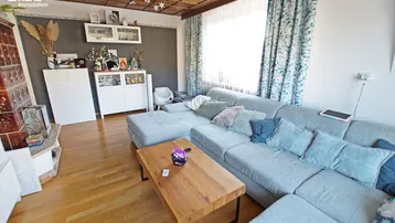 Gemütliches Wohnzimmer mit großem Ecksofa, Holzboden und traditionellem Kachelofen.