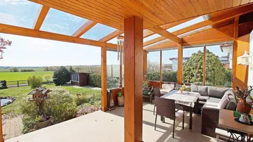 Überdachte Terrasse mit Holzdach, Glasfronten und weitem Blick ins Grüne, ideal für entspannte Stunden.