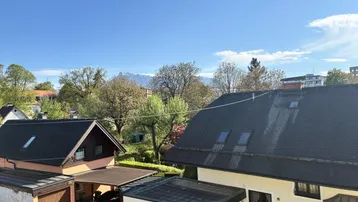 Blick über die Dächer der Nachbarschaft mit grüner Umgebung und Bergsicht unter blauem Himmel.
