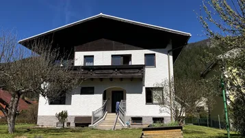 Vorderansicht eines Einfamilienhauses mit weißer Fassade und gepflegtem Vorgarten unter blauem Himmel.