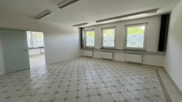 Geräumiger Büroraum mit hellen Fliesen, mehreren Fenstern und Schiebetür zu einem weiteren Bereich.