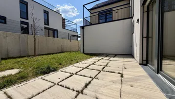 Gepflasterte Terrasse mit angrenzender Rasenfläche und Blick auf moderne Gebäude.