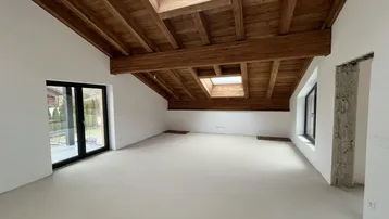 Heller Raum im Dachgeschoss mit sichtbaren Holzbalken, Dachfenstern und Zugang zum Garten.