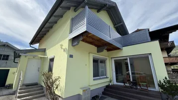 Ansicht des Hauses mit hellgelber Fassade, einem Balkon und einer kleinen Terrasse im Erdgeschoss.