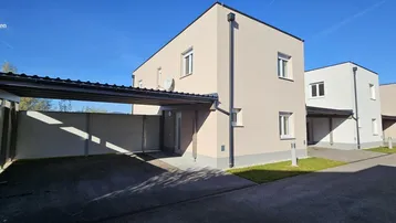 Moderne Reihenhäuser mit heller Fassade und überdachtem Carport unter blauem Himmel.