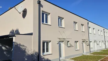 Moderne Reihenhäuser mit heller Fassade und Carport-Zugang unter blauem Himmel.