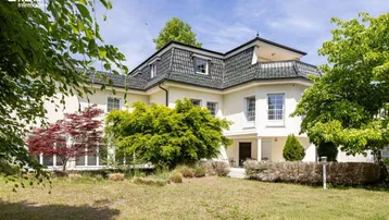 Großzügige Villa mit gepflegtem Vorgarten und klassischer Architektur unter blauem Himmel.
