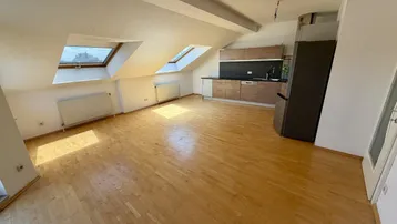 Helles Dachgeschosszimmer mit Holzboden, Dachfenstern und integrierter Küchenzeile.