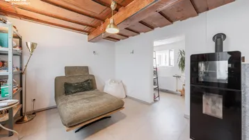 Wohnzimmer mit Holzbalkendecke, hellem Boden und modernem Kaminofen für gemütliche Abende.