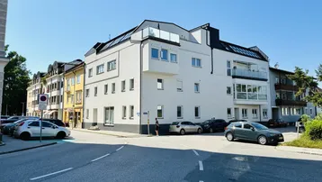 Modernes Mehrfamilienhaus mit weißer Fassade, großen Fenstern und mehreren Balkonen in städtischer Umgebung.