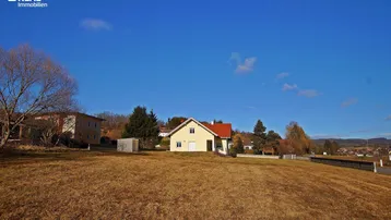 Weitläufige Ansicht des Einfamilienhauses in einer grünen, ländlichen Umgebung unter blauem Himmel.