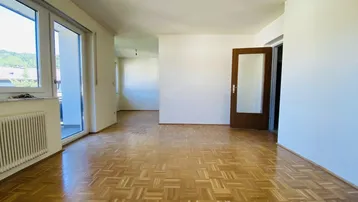 Helles Wohnzimmer mit Parkettboden, Balkonzugang und Blick ins Grüne.