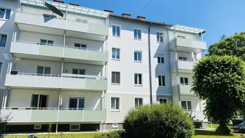 Mehrfamilienhaus mit mehreren Balkonen und gepflegter Grünfläche im Außenbereich.