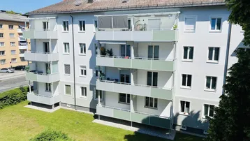 Mehrfamilienhaus mit mehreren Balkonen und einer grünen Rasenfläche im Vordergrund.