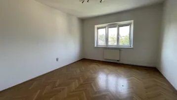 Geräumiger, heller Raum mit Fischgrätparkett, weißen Wänden und einem großen Fenster.