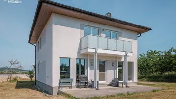 Modernes Einfamilienhaus mit Balkon und kleiner Terrasse im Gartenbereich.