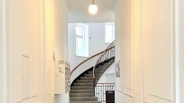 Heller Eingangsbereich eines Altbaus mit gemustertem Fliesenboden und geschwungener Treppe.
