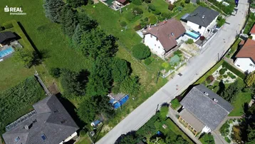 Luftaufnahme einer Wohnsiedlung mit Häusern, Gärten und einer Straße in ländlicher Umgebung.