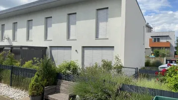Moderne Reihenhausfassade mit Jalousien und einem kleinen Vorgartenbereich mit Sitzbank.