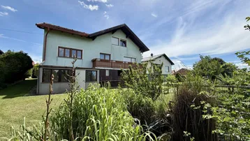 Ansicht des Hauses von hinten mit Gartenbereich und üppiger Vegetation unter blauem Himmel.