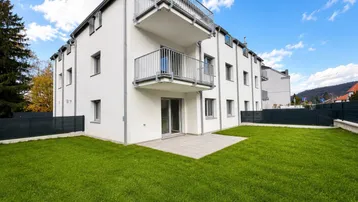 Modernes Mehrfamilienhaus mit weißer Fassade, Balkonen und einer kleinen Rasenfläche mit Terrasse.