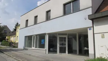 Modernes Geschäftsgebäude mit großen Schaufenstern und heller Fassade an einer Straße gelegen.