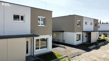 Moderne Reihenhäuser mit zweifarbiger Fassade und gepflegter Außenanlage unter blauem Himmel.