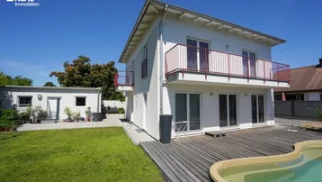 Weißes Einfamilienhaus mit Balkonen, Holzterrasse und einem kleinen Pool im Garten.