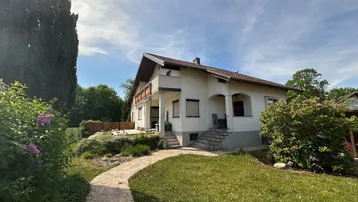 Charmantes Einfamilienhaus mit gepflegtem Vorgarten und Steinweg unter blauem Himmel.