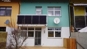 Fassade eines Reihenhauses mit Holzterrasse, Solarpaneelen und Satellitenschüssel.