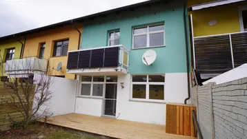 Rückseite eines Reihenhauses mit Holzterrasse, kleinem Garten und Solarpaneelen am Balkon.