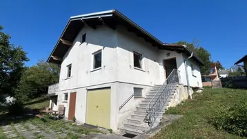 Freistehendes Haus mit Garage im Untergeschoss und Außentreppe zum Eingang.