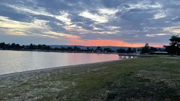 Malerischer Sonnenuntergang über dem See mit einem schmalen Strand und einer Bergkette am Horizont.