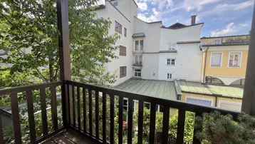 Blick vom Holzbalkon auf den begrünten Innenhof und die umliegenden Gebäude.